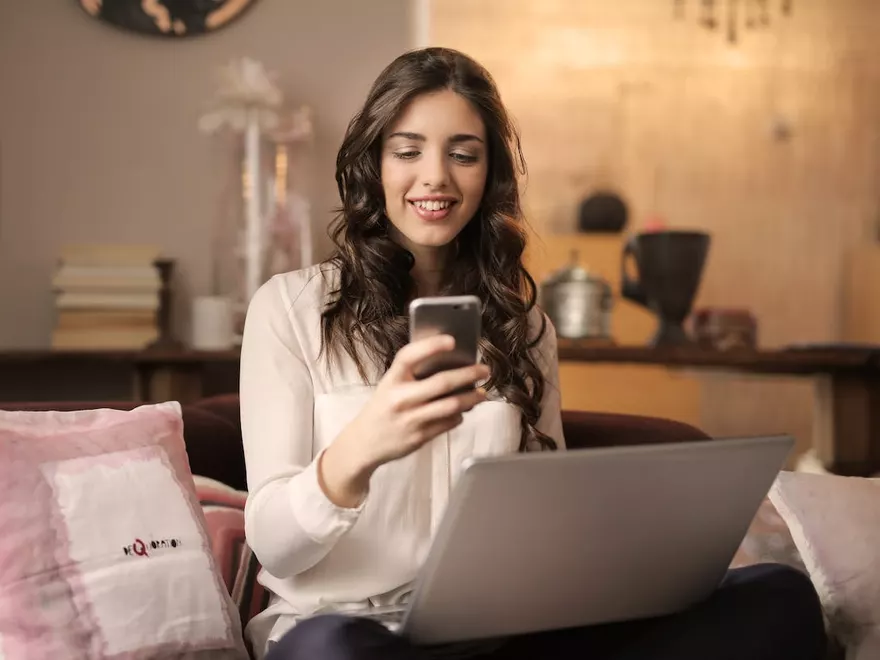 Frau mit Smartphone und Laptop auf dem Sofa